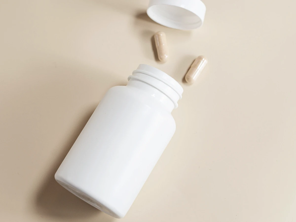 A plain white supplement bottle with capsules beside it