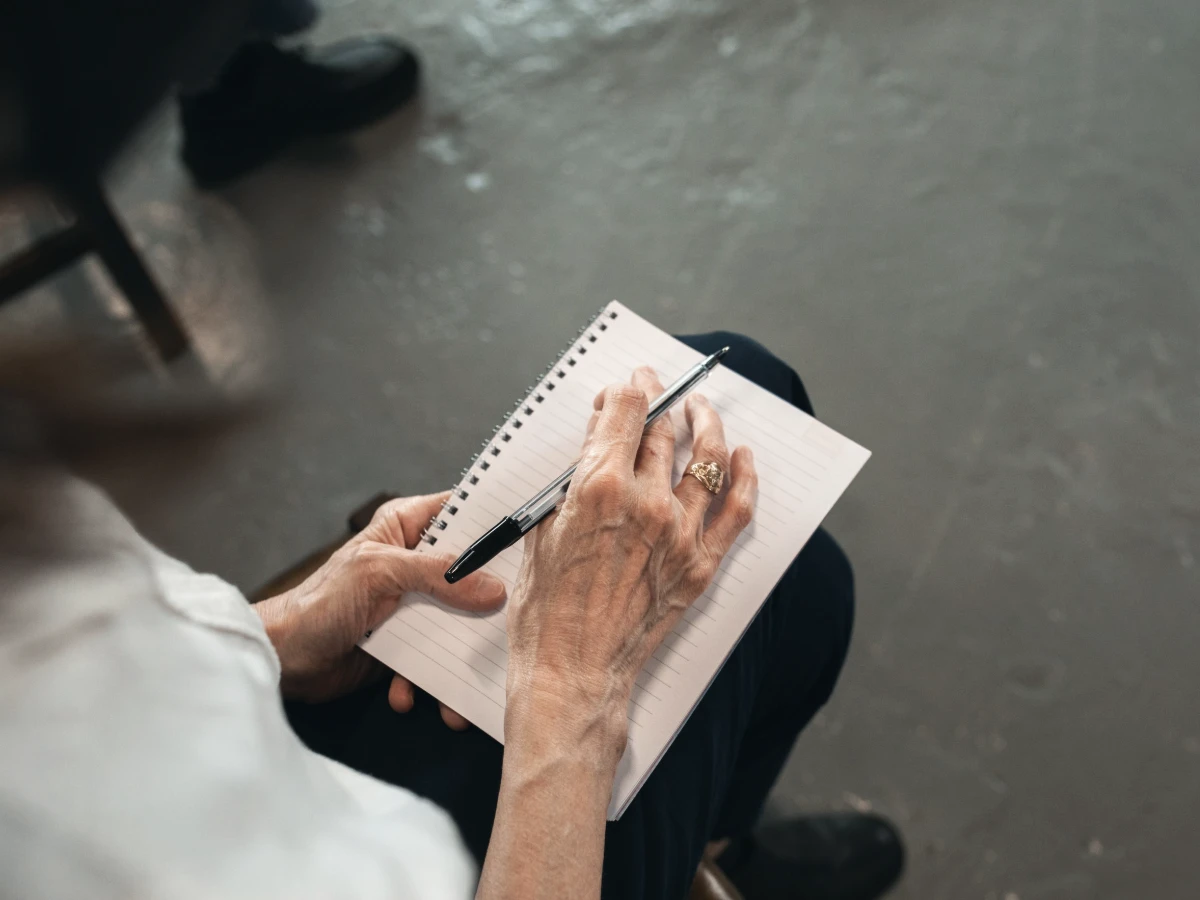 Older hands writing a list of questions in a spiral notebook before an appointment