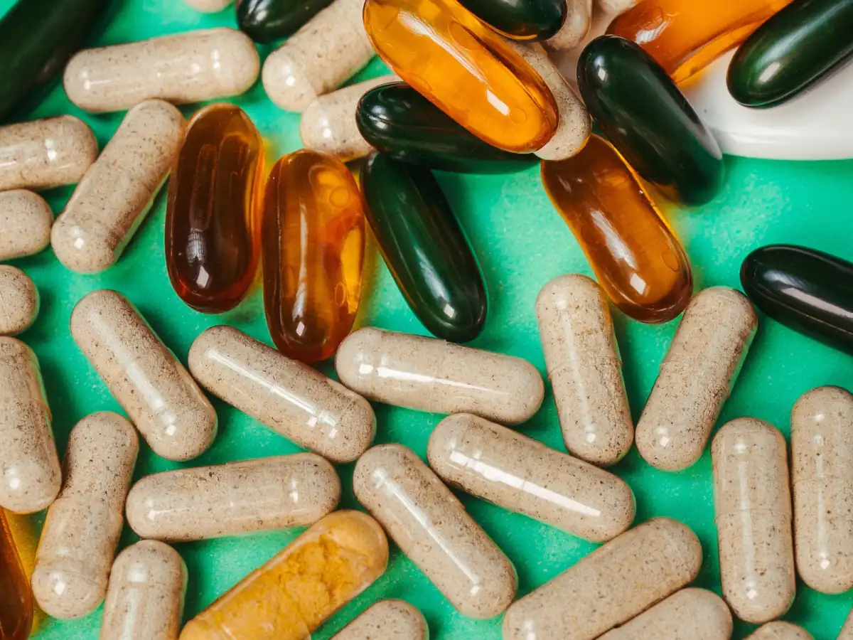 Supplement capsules and softgels scattered across a green surface
