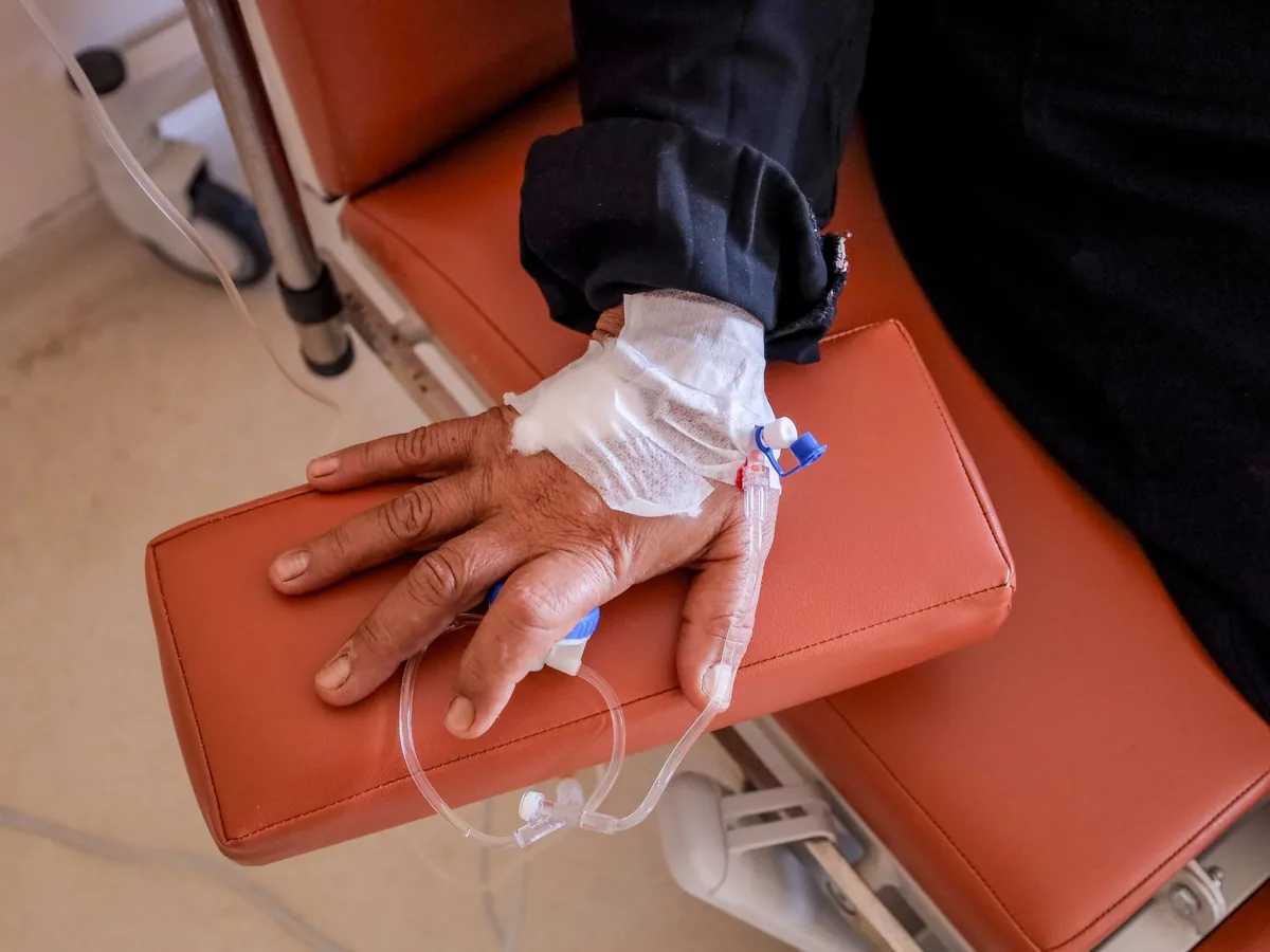 A patient’s hand with an intravenous line taped in place, resting on the arm of a treatment chair