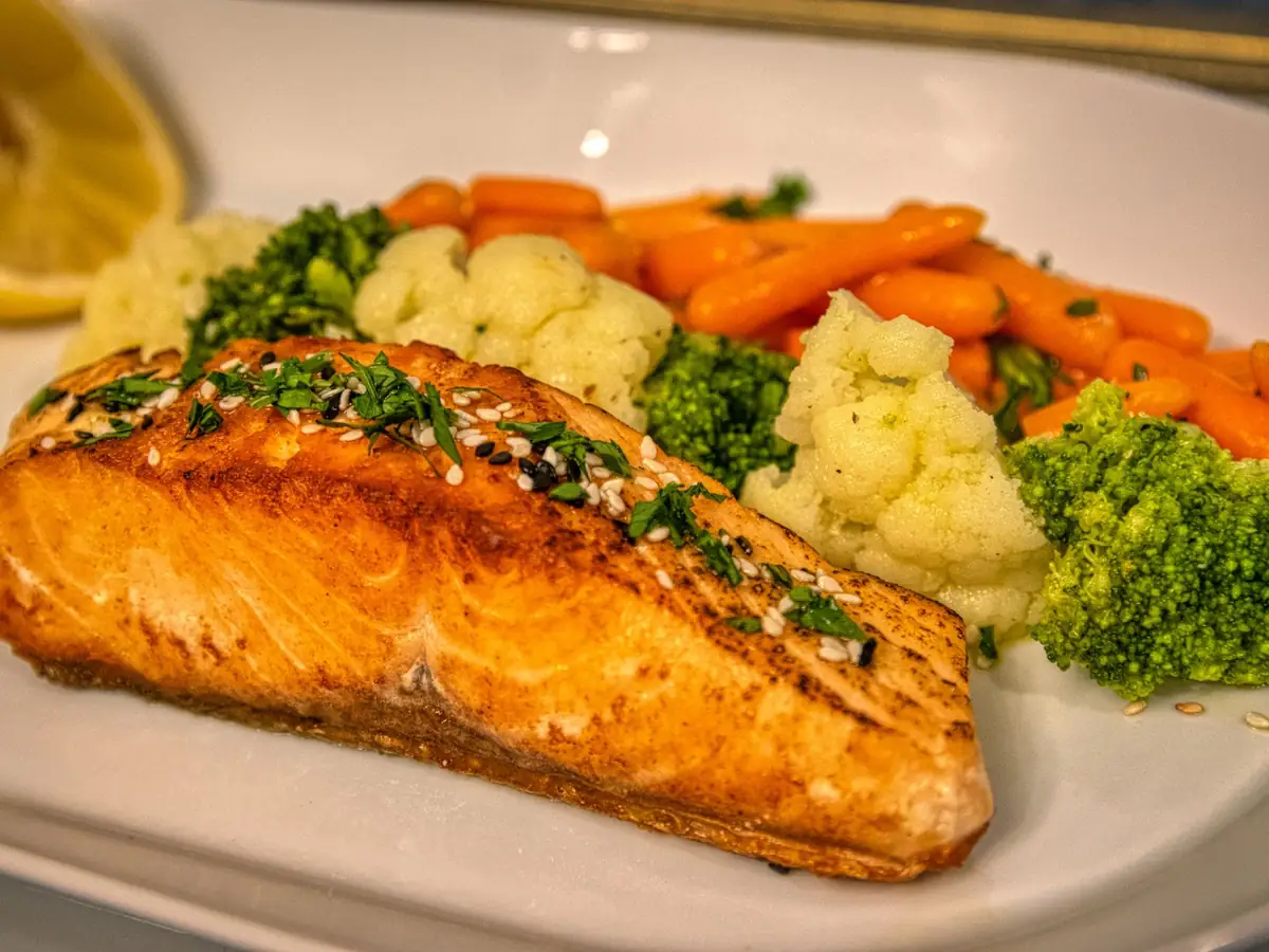 A plate of grilled salmon with broccoli, cauliflower and carrots