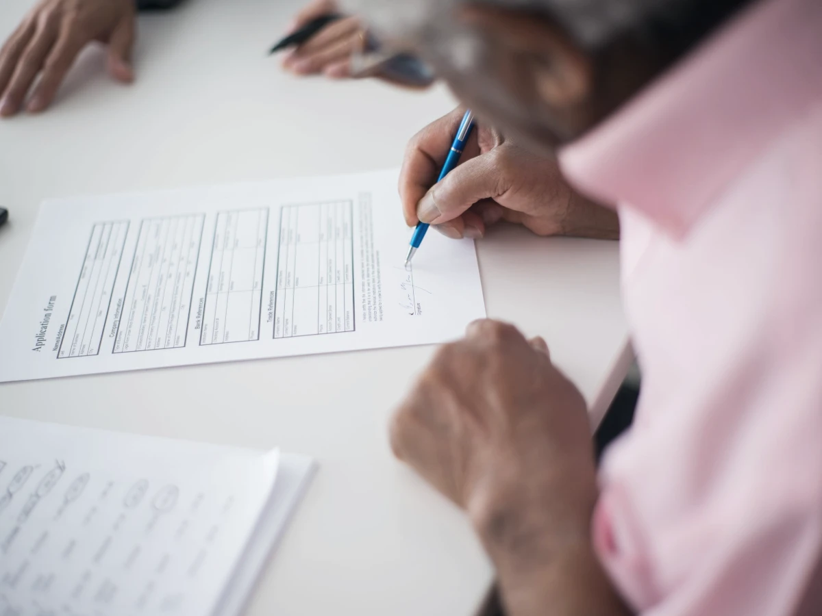 An older man completing and signing an application form at a desk