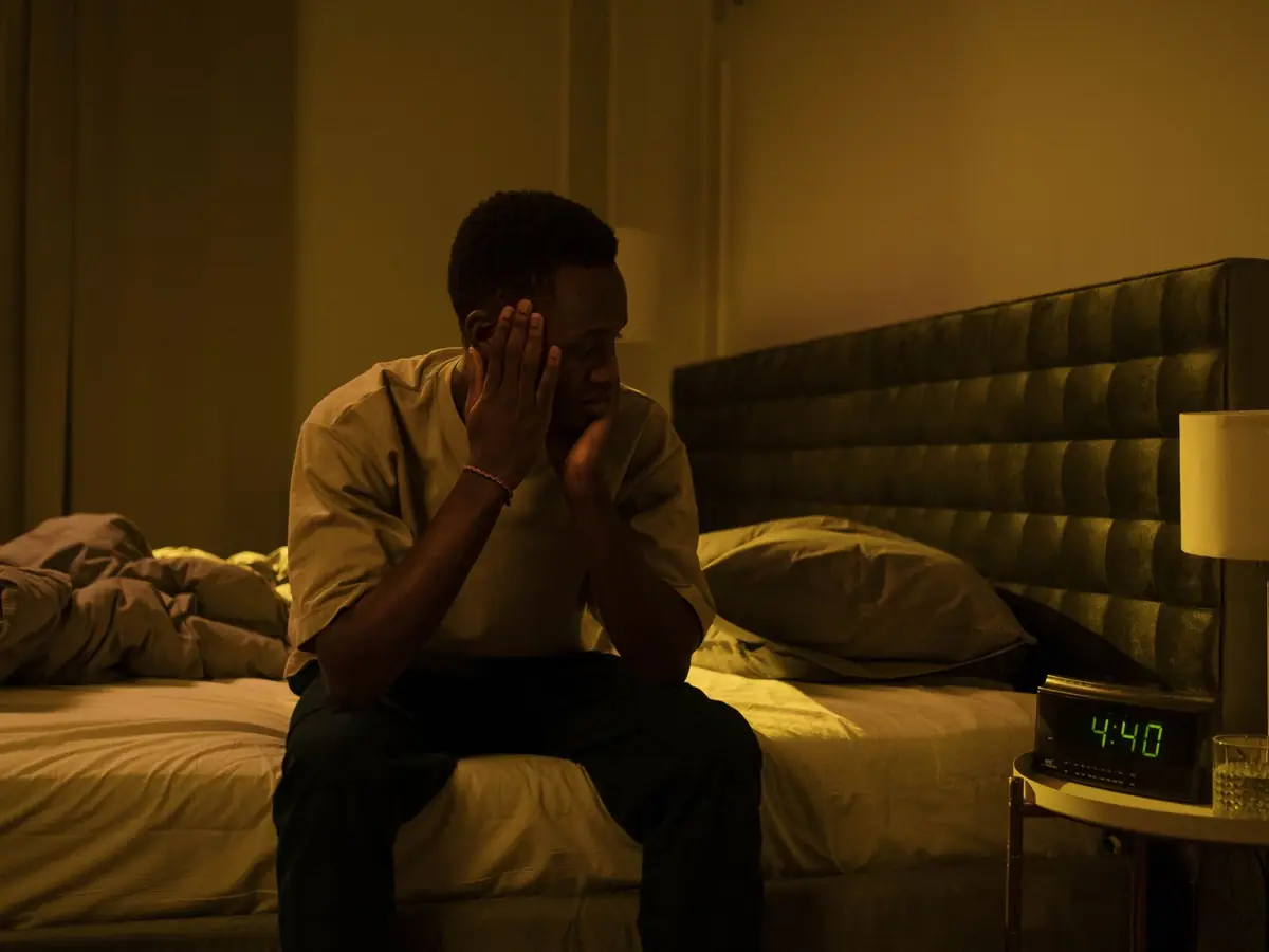 A man sitting on the edge of his bed at 4:40 in the morning with his head in his hands