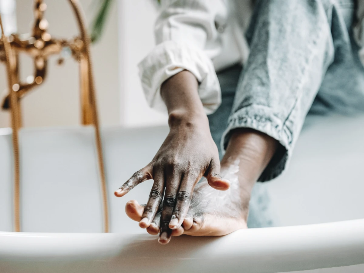 Hands applying cream to a bare foot while seated on the edge of a bath