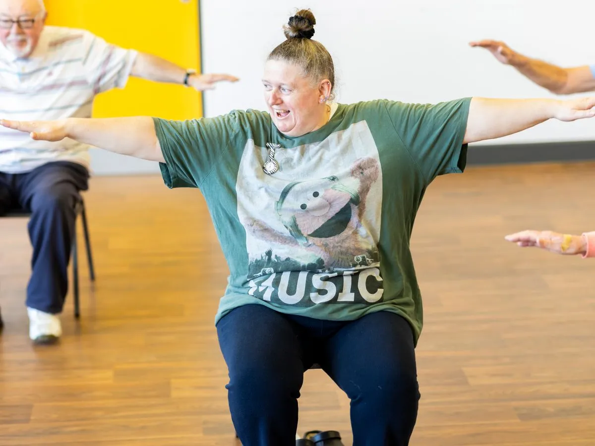 Older adults doing a seated exercise class with their arms stretched out to the sides