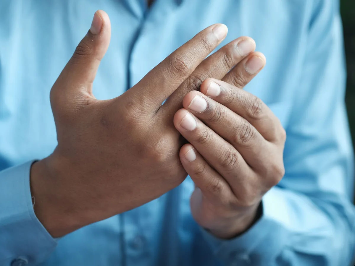 A man in a blue shirt pressing and rubbing one hand with the other