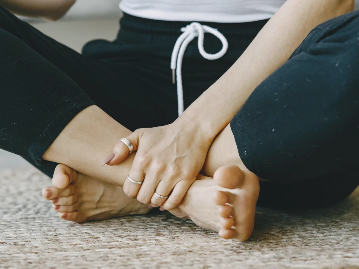 A seated person holding their own bare foot on a rug