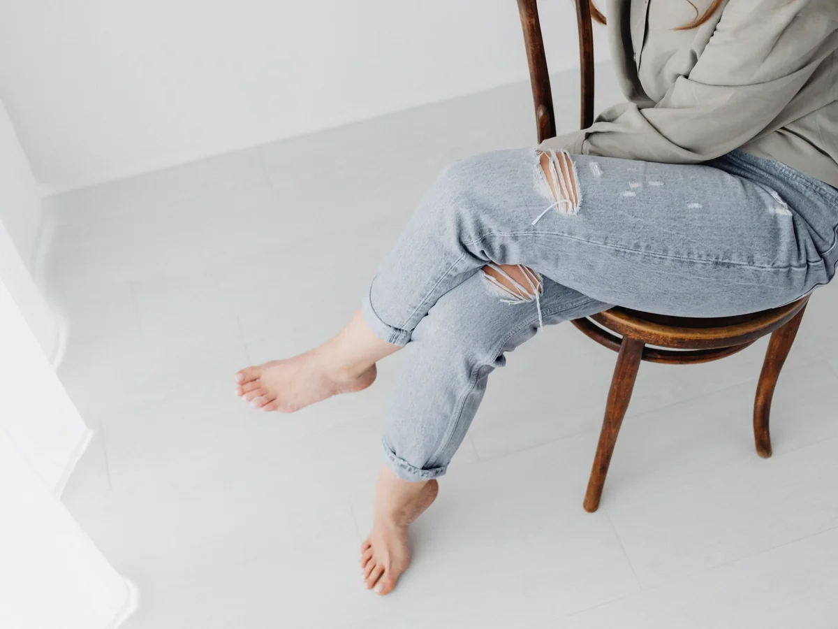 A person sitting on a wooden chair with one leg crossed over the other knee