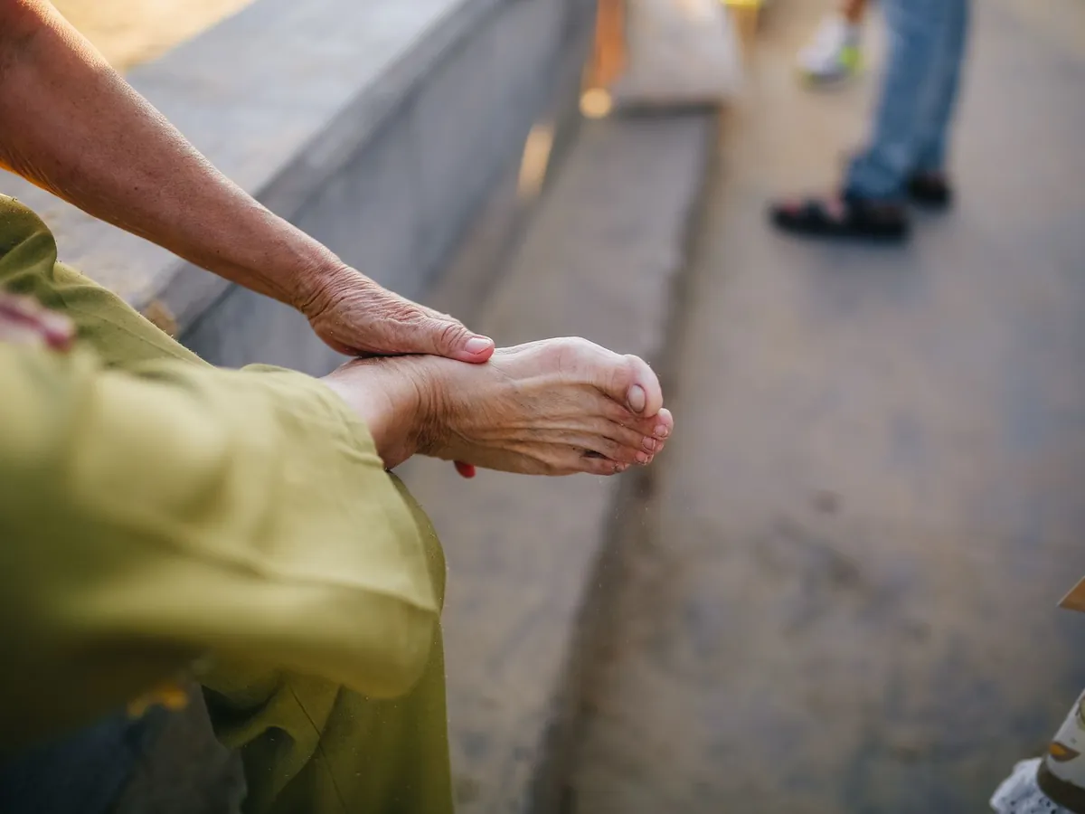 An older adult sitting on a step and rubbing a bare foot