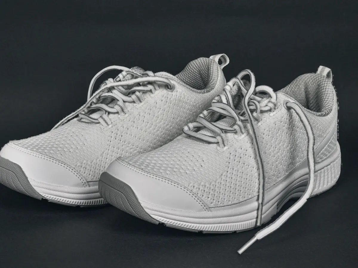 A pair of wide, cushioned lace-up walking shoes photographed on a dark background