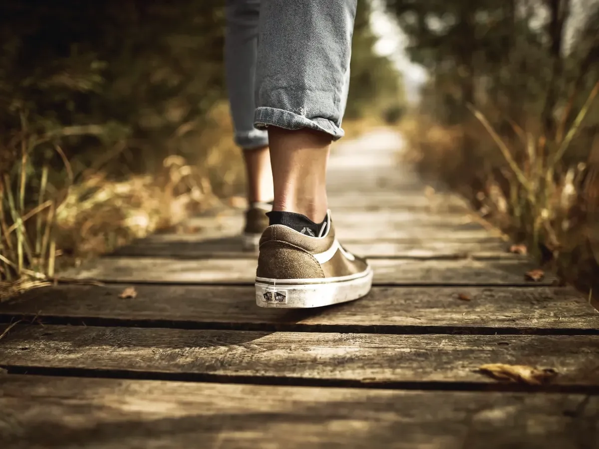 A person walking along a wooden boardwalk in low afternoon sunlight