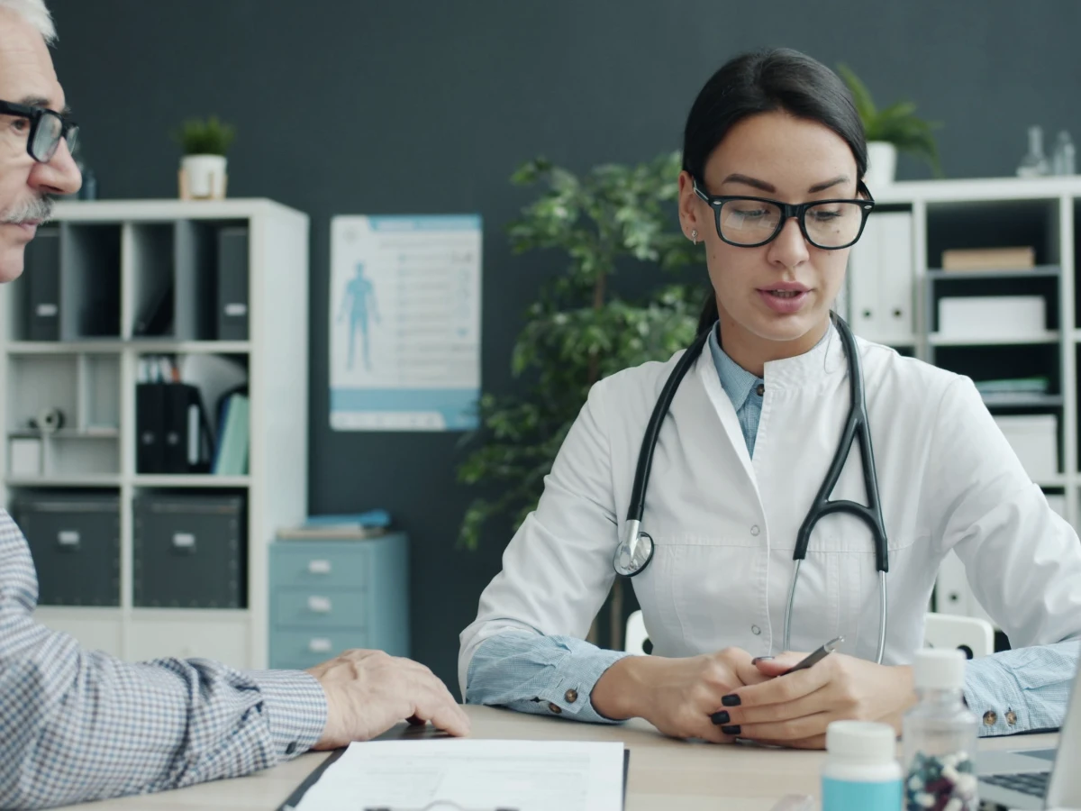 An older man reviewing treatment options with a doctor across a desk in a consulting room
