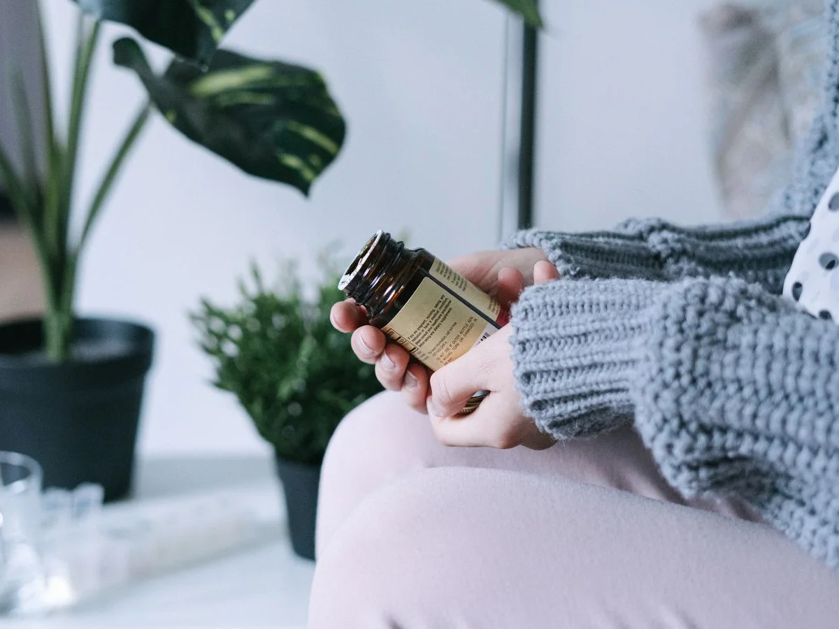 Hands in a gray knit sweater turning an amber supplement bottle to read the back label