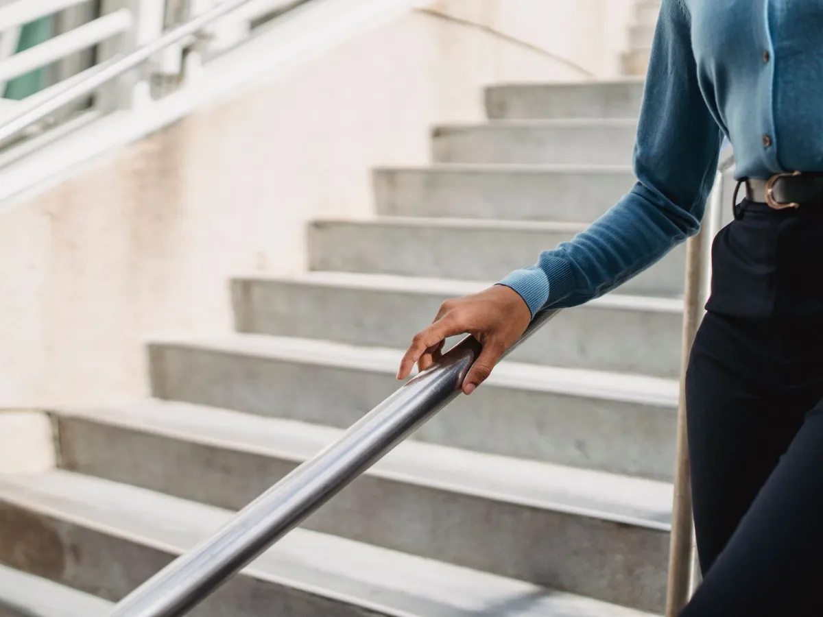 A hand resting on a metal handrail beside a flight of pale concrete stairs