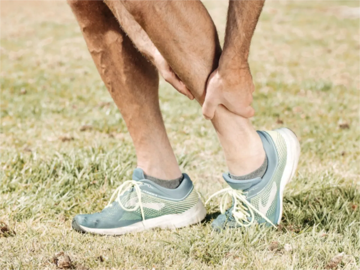 A man in running shoes holding his calf with both hands