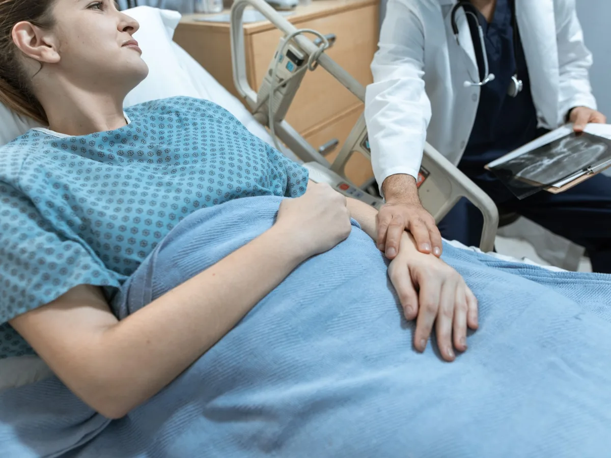 A doctor resting a hand on the arm of a patient lying in a hospital bed