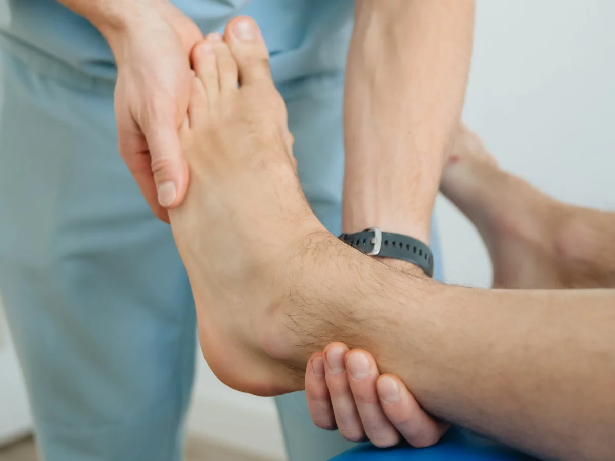 A clinician’s hands supporting a patient’s bare foot and ankle during an examination on a treatment table